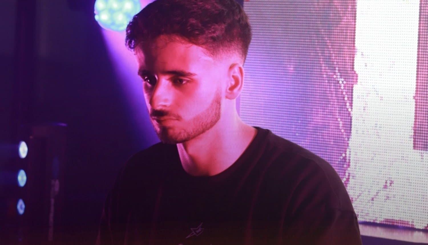 Disak in the Kalor DJ booth, with purple light and a projector behind