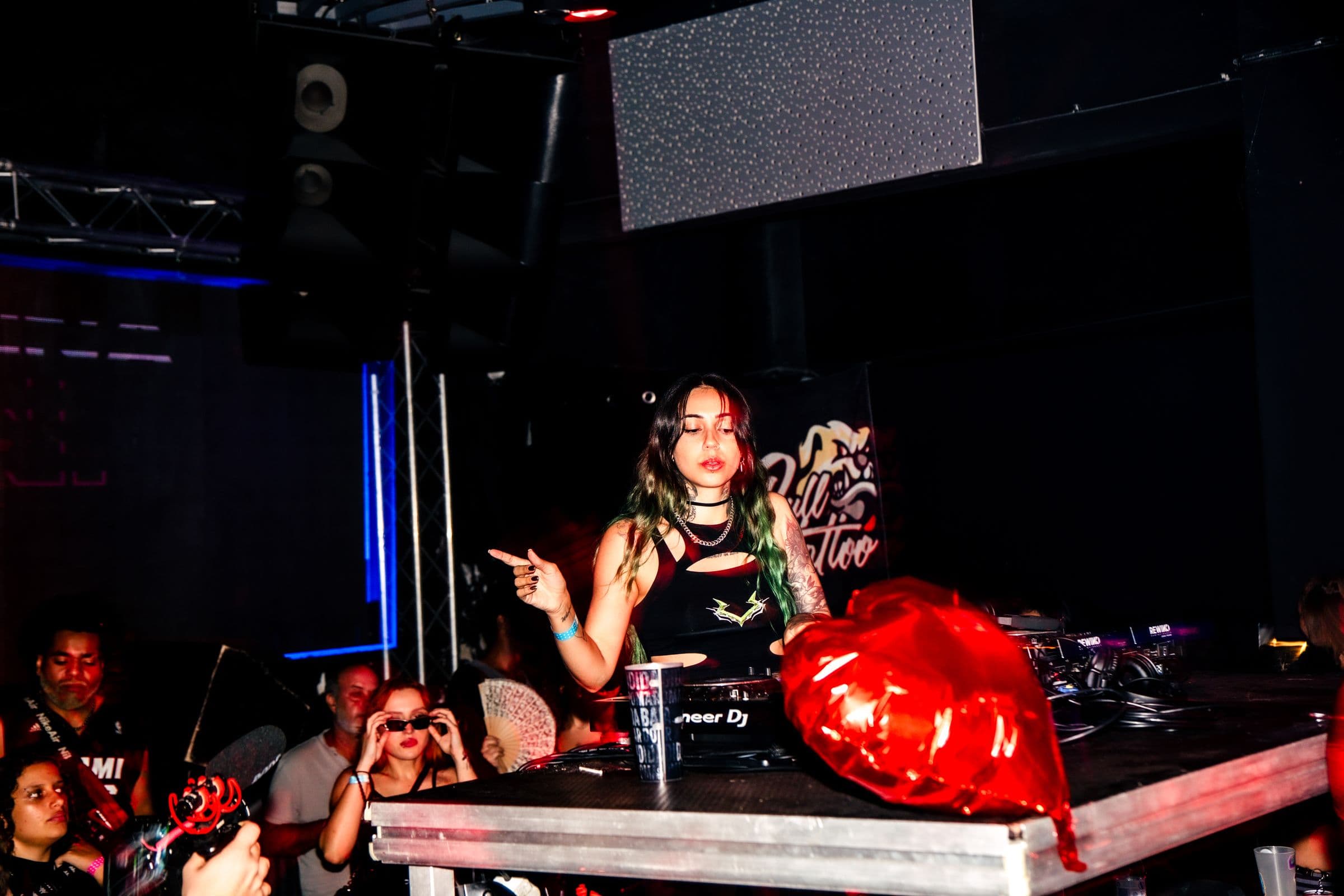 DJ do HER atrás da mesa, com balões de coração vermelhos e luz da pista